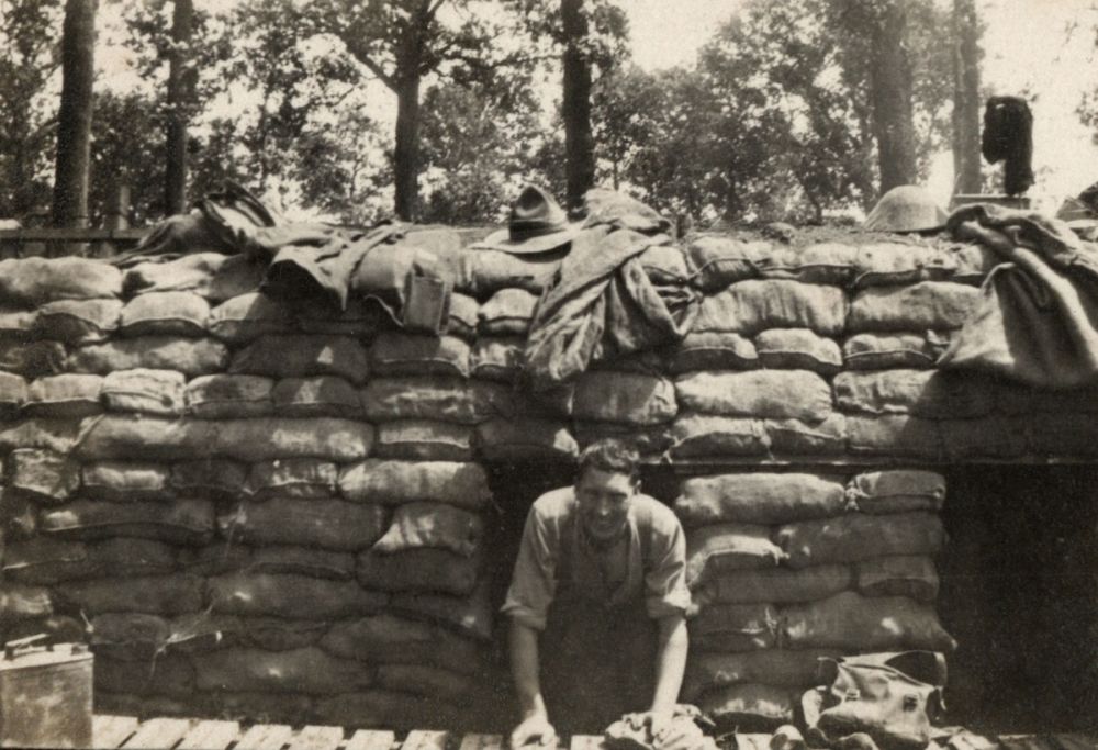 A smiling soldier poses halfway out of his sandbagged bunker named Mud Lane Breastwork. Ploegsteert, Belgium, Winter 1917/18